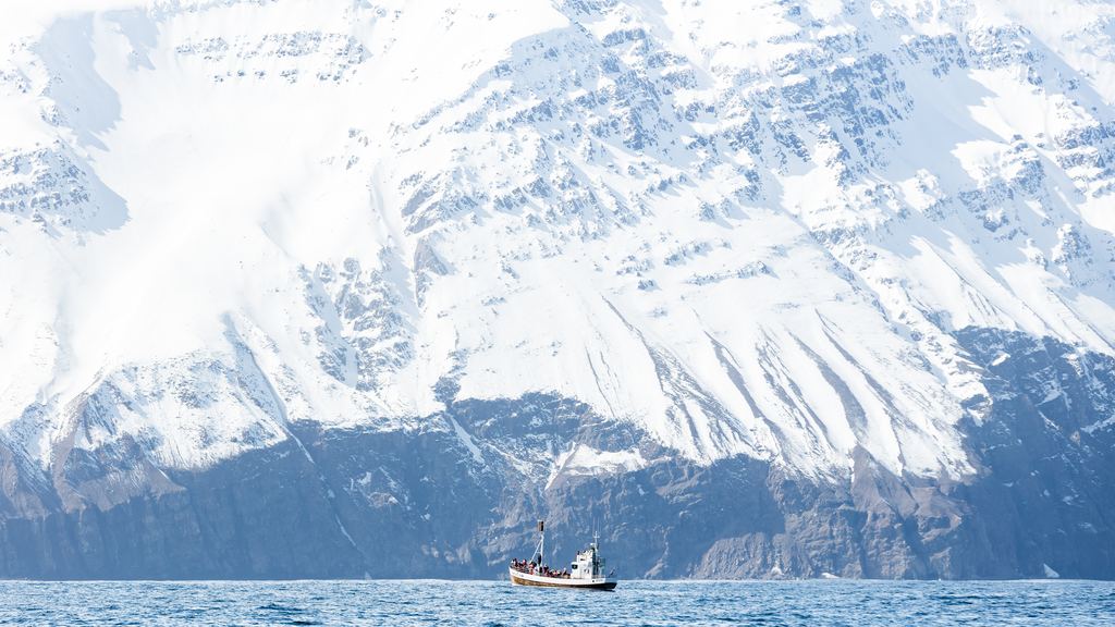 A small boat on dark water below steep snow covered mountains near Tromsø