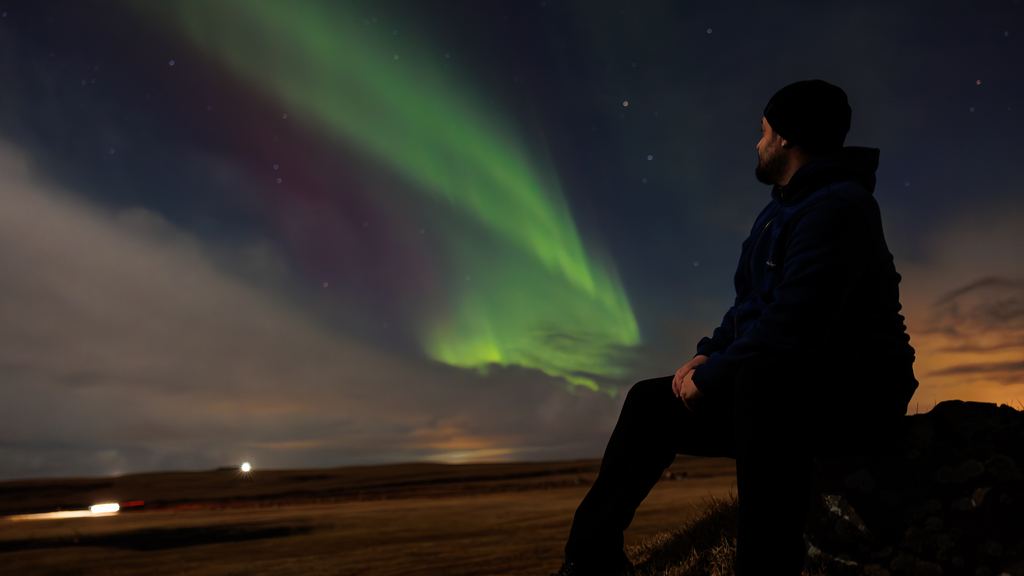 A traveller in the snow watching a bright green aurora overhead