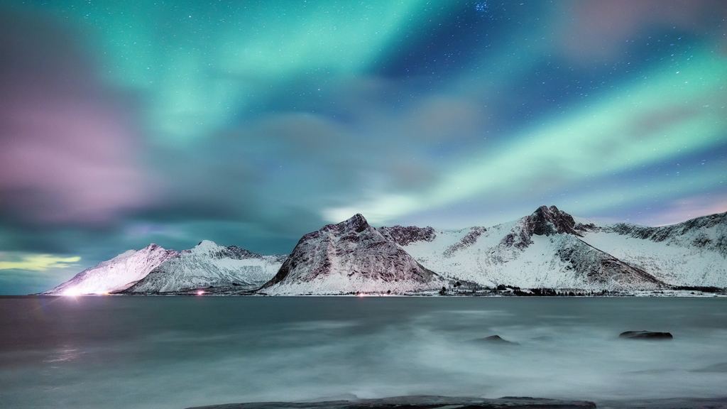 Green aurora and broken cloud above snow covered peaks and the sea at Senja, northern Norway