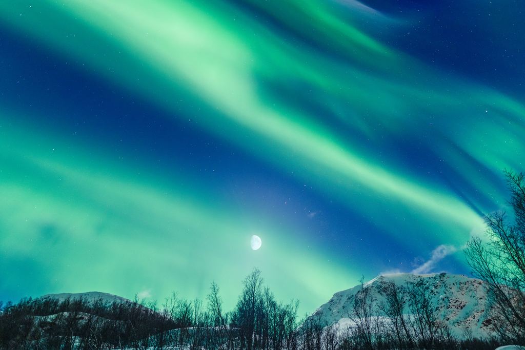 Aurora and a bright moon share the same winter sky above snow and low hills near Tromso