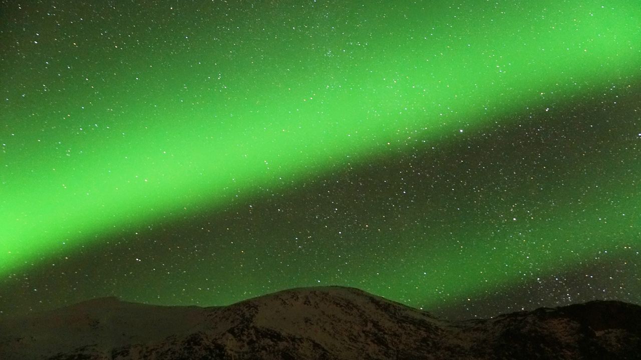 Two green aurora bands crossing a star filled sky above a snowy ridge inside the Arctic Circle in northern Norway
