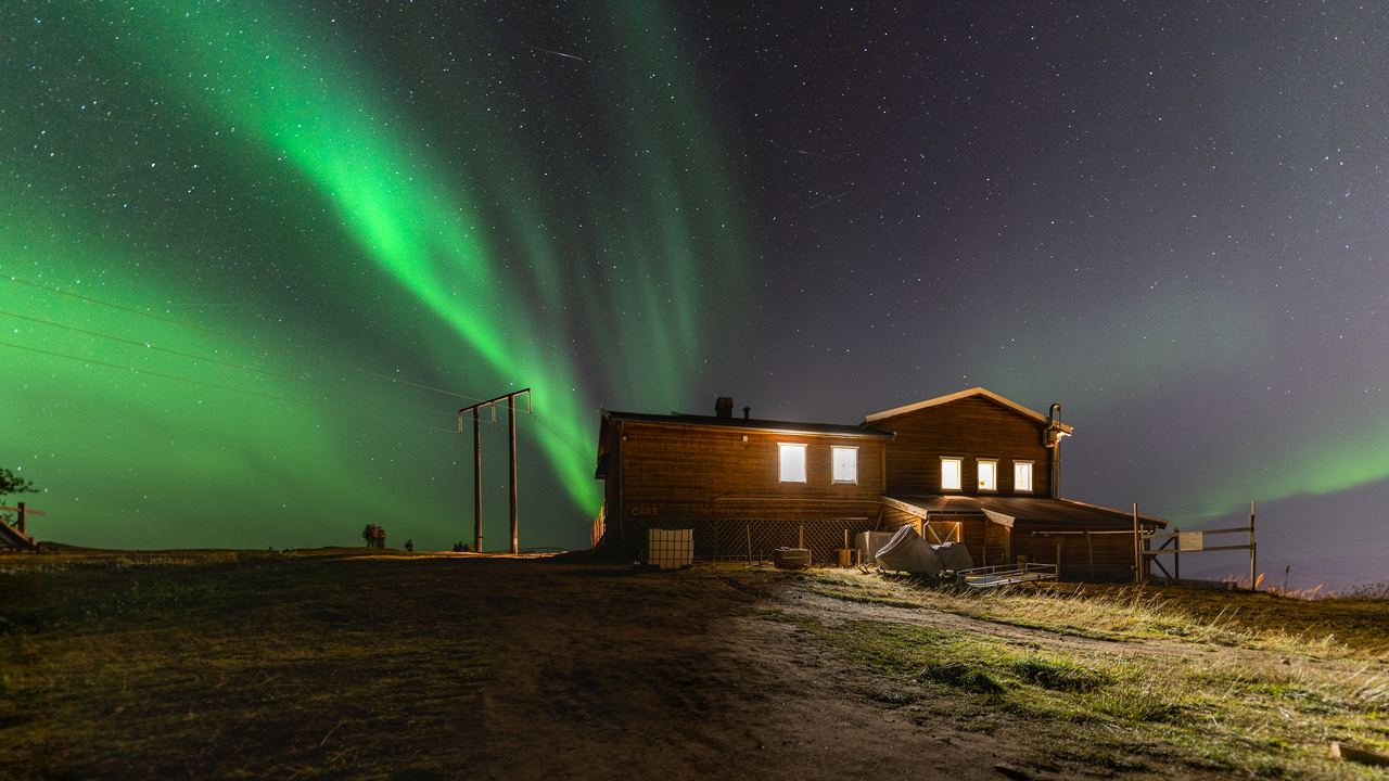 Green aurora above a snow covered coastline and dark water in northern Norway on a clear night
