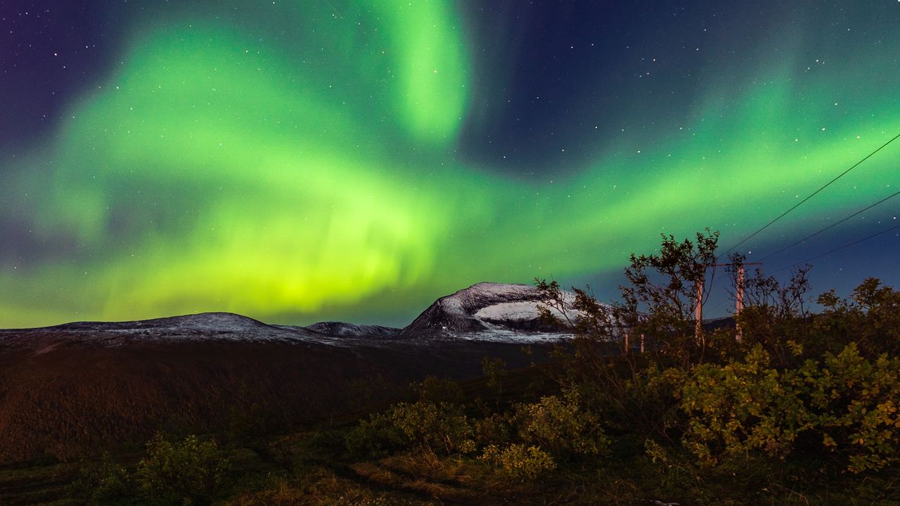 Green aurora arcs across the night sky above snow-covered peaks on the Norwegian coast