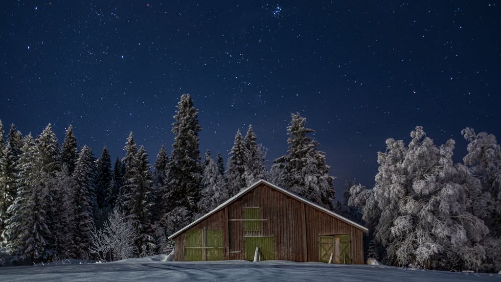 A small wooden cabin in a snowy forest at night, under a sky full of stars