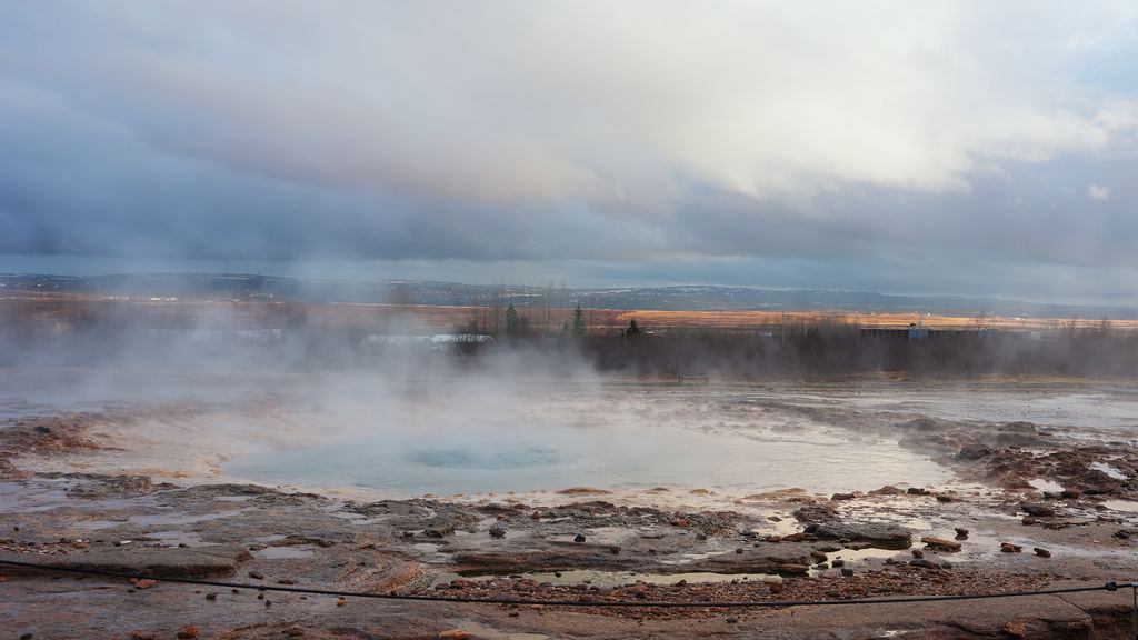 A geyser erupting in an open Icelandic landscape, throwing hot water and steam into the air
