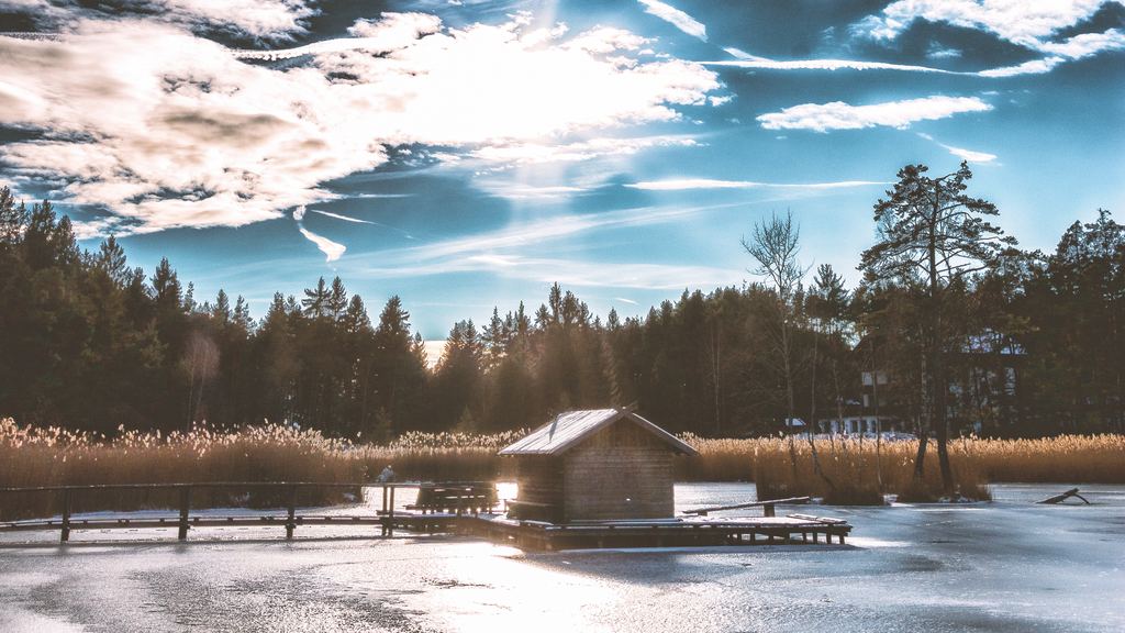 A small wooden hut standing on the ice of a frozen lake in winter