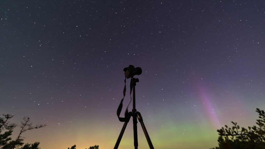 A camera on a tripod pointed at a starry sky with faint aurora