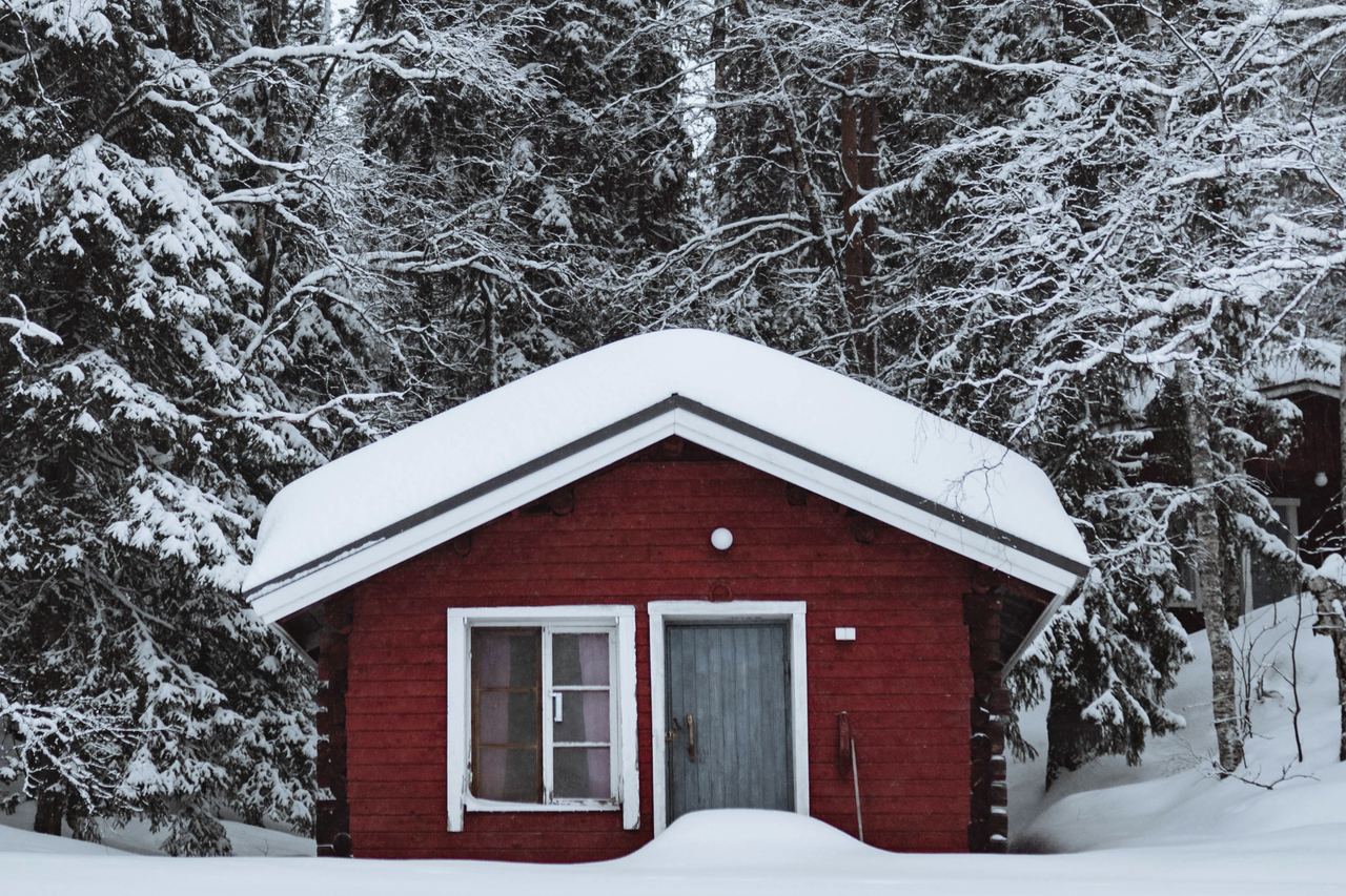 A red-painted wooden cabin standing in deep snow among winter trees
