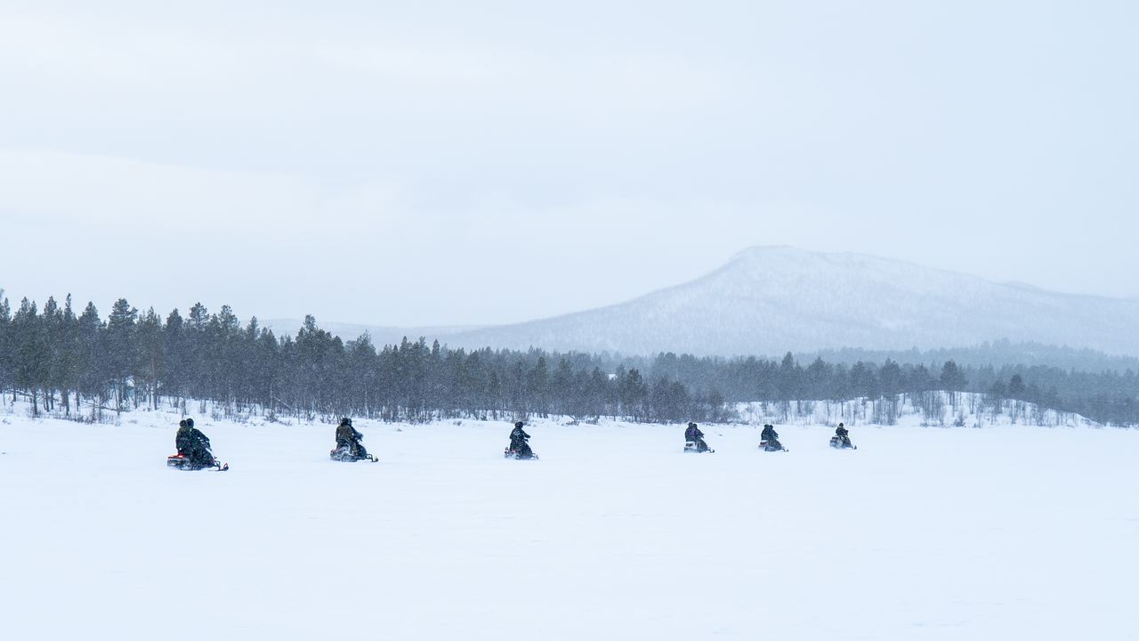 Riders on snowmobiles crossing open snow in northern Sweden